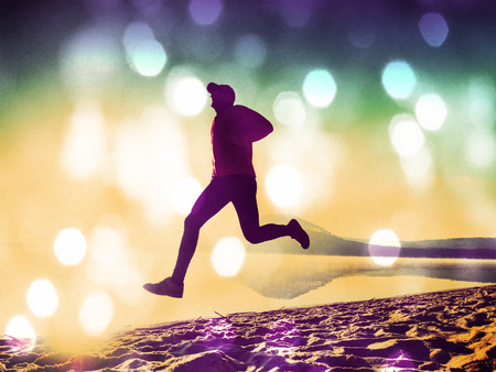 Film grain effect. Man exercising on the beach.  Silhouette of active man exercising  and stretching on the lake beach at sunrise. Healthy lifestyle.の写真素材