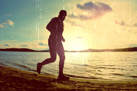 Film grain effect.  Tall man with sunglass and dark cap is  running on the beach at sunsetの写真素材