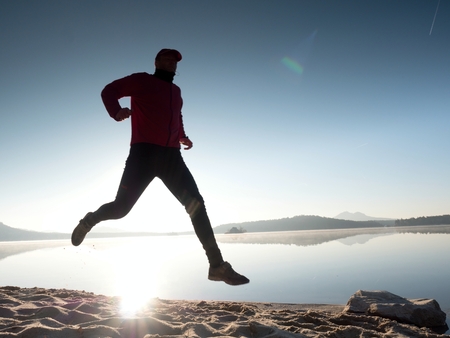 Running man. Boy fast running on the morning beach. Sportsman runner, jogging guy during sunrise over sandy beachの写真素材