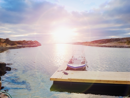 Fishing boat at sunset calm water. A motorboat for sport fishing tied to a wooden floating dock.の写真素材