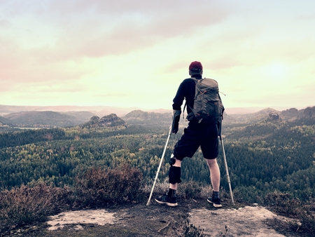 Disabled tourist on crutches on rock. Hurt knee in neoprene metal knee braces and man hold forearms crutches.の写真素材