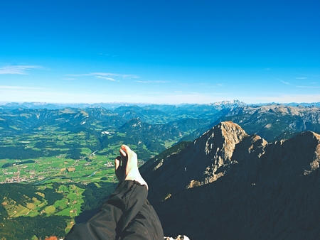 Tired male legs in dark outdoor trousers on peak of mountain above valley. Rest in hike in the mountains. Naked feets without boots on the background of the Alps peaksの写真素材