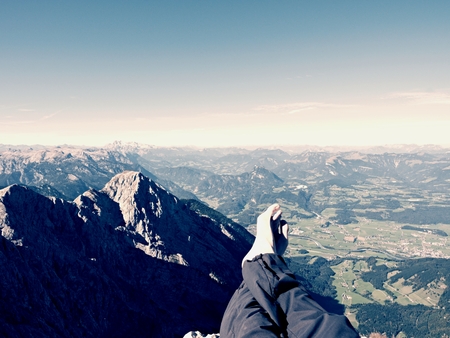 Tired male legs in dark outdoor trousers on peak of mountain above valley. Rest in hike in the mountains. Naked feets without boots on the background of the Alps peaksの写真素材