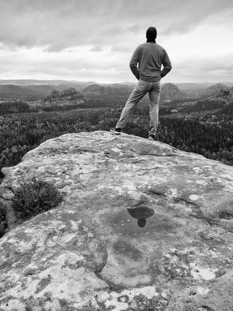 Hiker man stays on a rocky ridge and enjoy view over long valley to horizon. Cold Sun hidden in clouds. National park with a  rocky mountains and  valleys.の写真素材