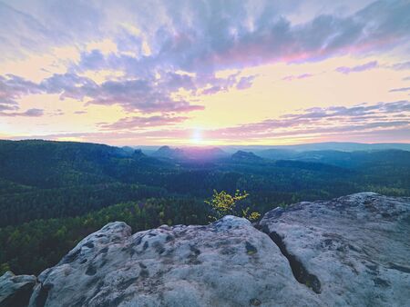Spring morning nature. The cracked sandstone cliff above forest valley, daybreak Sun at horizon. Hills increased from misty backgroundの写真素材