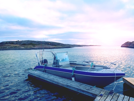 Fishing boat in bay port, sunset calm water. A motorboat for sport fishing tied to a wooden floating dock.の写真素材