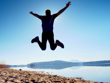 Jumping man. Sportsman crazy jumping  and jogging on beach during the sunrise above horizonの写真素材