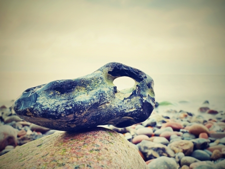 Bizzare stones on costline, the stony beach ends in smooth water of blurred ocean. Colorful sky aboveの写真素材
