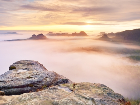 View over sharp sandstone edge into long valley full of first autumnal mist. The misty forest valley of national park in germany with the sandstone rock in the foregroundの写真素材