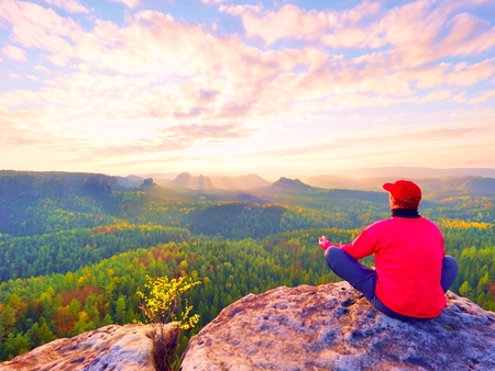 Single man tourist  sit on rock empire. View point with exposed rocky peak above valley. Sunny daybreak in rocky mountains.の写真素材