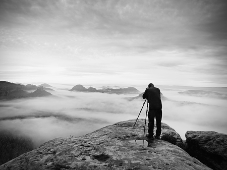 Photographer framing picture with eye on viewfinder. Photo enthusiast  enjoy work of fall nature on rocky summit. Dreamy landscape, misty sunrise in a beautiful valley belowの写真素材