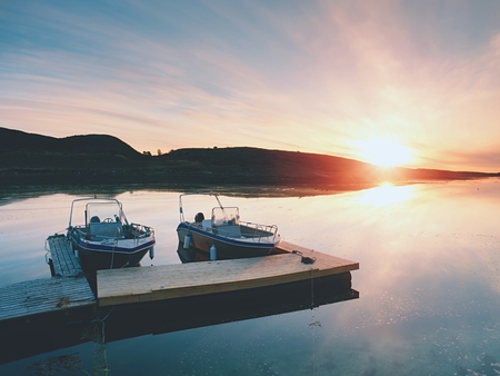 Fihing boat docked in the harbor at floating wooden pier. Background beautiful sky with orange Sun.の写真素材