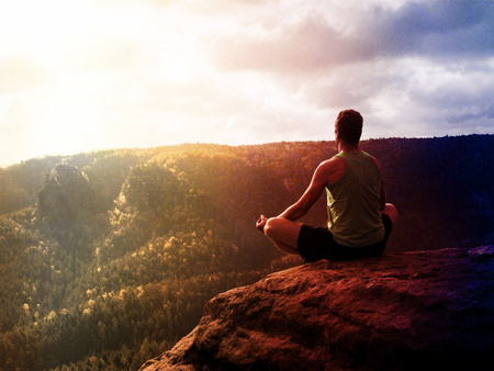 Lens defect. Man meditating in Lotus Pose on rocky cliff. Sportsman practicing Yoga on stone edge above landscapeの写真素材