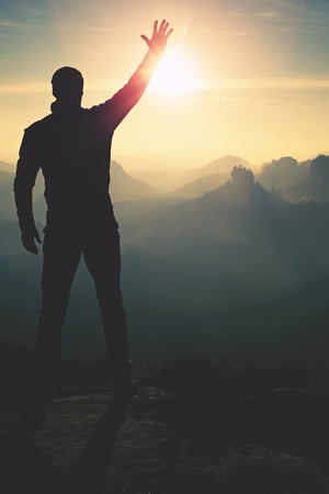 Man takes photos with phone on rock empire. Dreamy fogy mountains, spring orange pink misty sunrise in a beautiful valley of rocky mountains.の写真素材