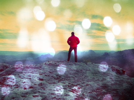 Lens defect. The figure of the men in red outdoor jacket on sharp cliff. Mountains within early fall daybreak. Conceptual scene.の写真素材
