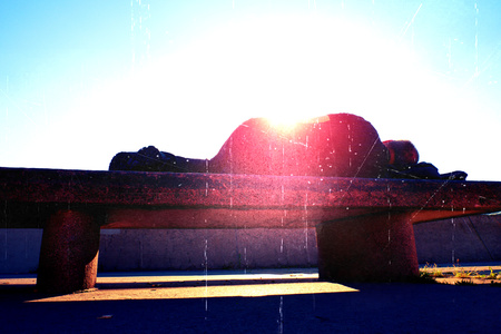 Flare, soft focus. Silhouette in sunbath. Drank adult man resting on stony bench in park, Sharp sun rays make contours around sleeping body.の写真素材