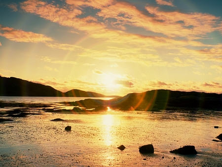 Walk within sunset on beach. Mirroring of  sunsetting horizon in sea water between rocks . Smooth...