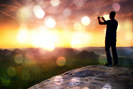 Flare, soft focus.Tall backpacker with phone in hand makes selfie. Sunny spring daybreak in rocky...