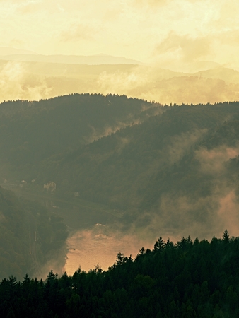 Cold and damp morning in autumn nature.  Outlines of forest hills hidden in thick mist. Unclear view to contours of hilly sides and peaks.の写真素材