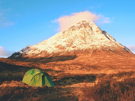 Green turistic tent on a meadow at the river below snowy cone of mountain Stob Dearg 1021 meters high. Higland in Scotland. A wonderful sunny winter day. Dry grass and heather bushes. Hikers tentの写真素材