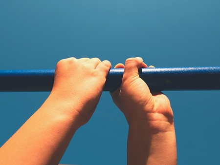 Boy hands holding on blue steel in outdoor  playground, blue sky in backgroundの写真素材