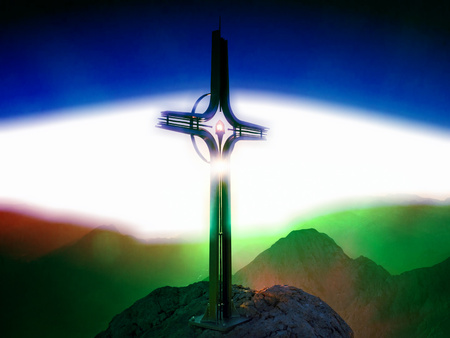 Flare, soft focus. Cross raised  at mountain summit. Sharp peak, daybreak Sun in sky. Steel crucifix in memory of victims of mountainsの写真素材