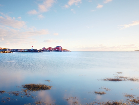 Red houses of the fishing village. Red white buildings  and lighthouse  in small port, coastline of cold north sea, Norway.の写真素材