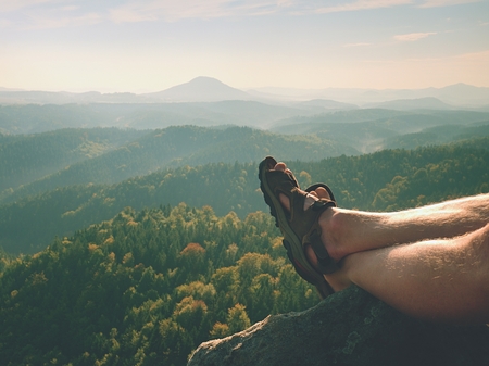 Long tired naked legs in hiking sandals on peak. Hiking in sandstone rocks, hilly landscape in blue...