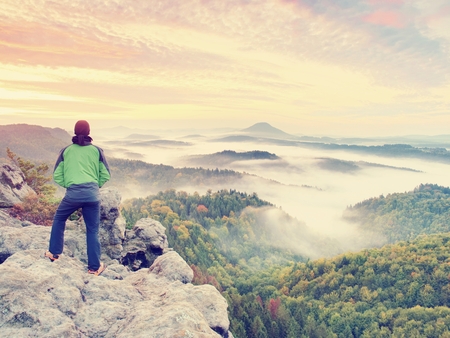 Man stay on rocky peak within daybreak and watch over misty landscape.  Beautiful autumn morning. 