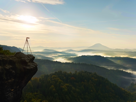 Tripod  with camera on view point ready for photography. Exposed rocky edge above landscape. Misty autumnal day  in wild nature. の写真素材