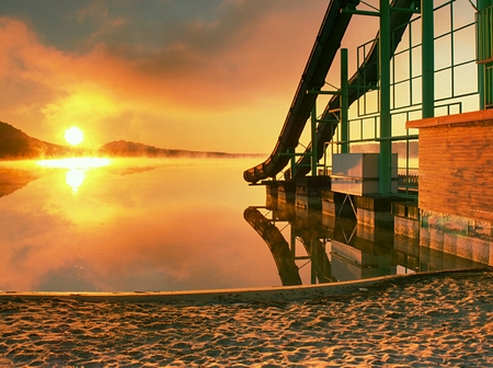 High steel tower with  sliding track on lake beach. Cold autumn morning with misty water level. End of season in  natural swimming resortの写真素材