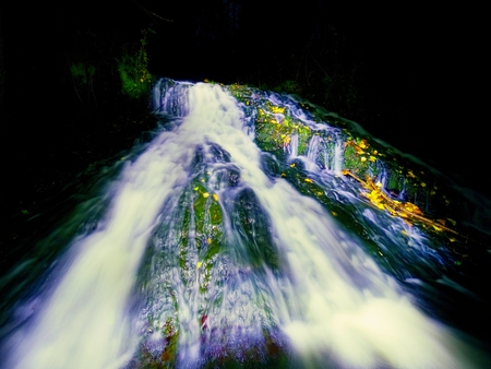 Light painting in night waterfall. White waterfall on mountain stream.  Blurred foamy water on mossy rock. The spray create on level and gravel milky waterの写真素材