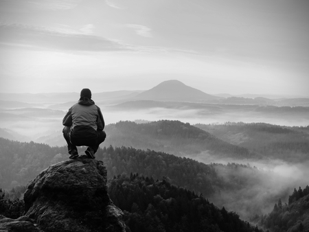 Man standing on rocky peak during daybreak and watch over misty landscape. Beautiful autumn morning.の写真素材