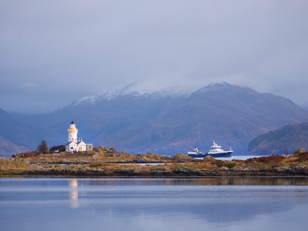 Lighthouse on Isle of Ornsay, the southern side of Isle of Skye, Scotland. Trade ship at rocky island, mountains in backgroundの写真素材
