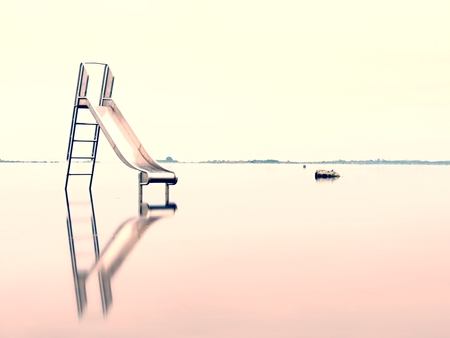 Sunset shore and old steel slide in lake. Chrome ladder tower with  sliding track, big granite...