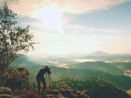 Nature photographer in the action.  Man silhouette above a misty clouds,  morning hilly landscape.の写真素材