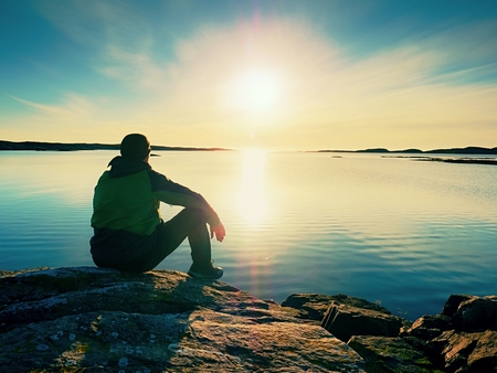 Lonely man hiker sits alone on the rocky  coast and  enjoying sunset. View over rocky cliff to free oceanの写真素材