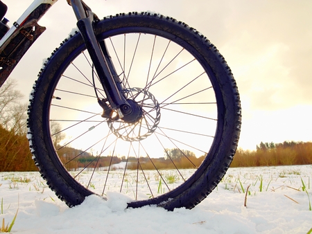 Front wheel of mountain bike stay in snow. Snow flakes melting on dark off road tyre.  Winter weather in the field.の写真素材