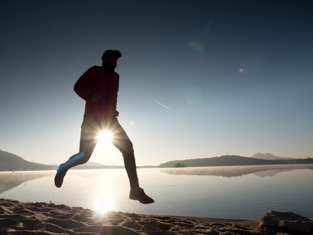 Exercising on the lake beach at sunset, big sun at horizonの写真素材