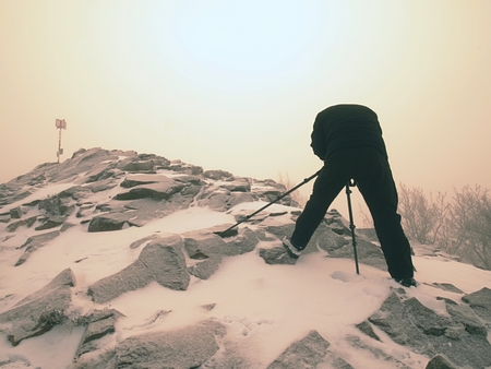 Travel photographer doing pictures in ancient stones on snowy peak of mountain. Winter cold and...