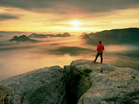 Hiker enjoy amazing view over heavy clouds. Mountain rocky peak above valley.
