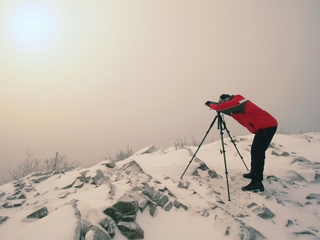 Travel photographer doing pictures in ancient stones on snowy peak of mountain. Winter cold and misty morning in mountainsの写真素材