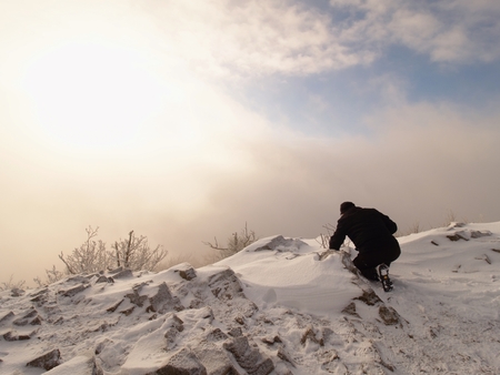 Photographer lay in snow on mountain peak and takes a picture of fantastic landscape around, snowy winter dayの写真素材