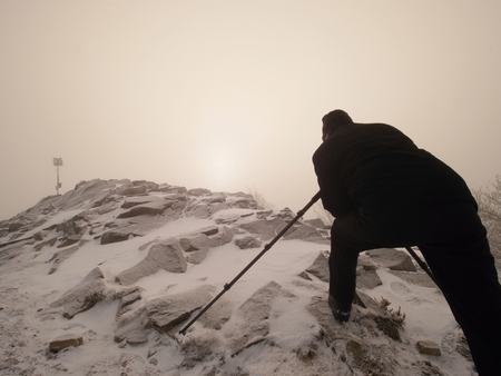 Professional photographer lay down to snow and takes photos with mirror camera on peak of snowy rock. . Man lay with big mirror camera on neck. Snowy rocky peak of mountain.の写真素材