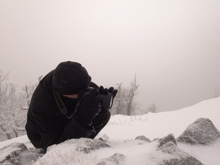Photographer lay in snow on mountain peak and takes a picture of fantastic landscape around, snowy winter dayの写真素材