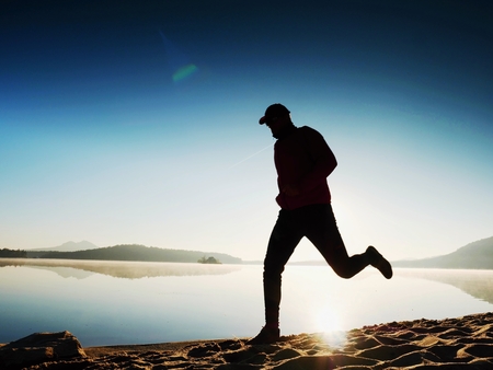 Close  silhouette of a runner man running along on the beach at sunset with sun in the background. Vintage effect style pictures.の写真素材