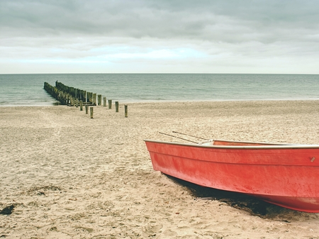 Abandoned red paddle boat on sandy beach of sea.  Smooth water level within morning windless. Dramatic and picturesque scene. の写真素材