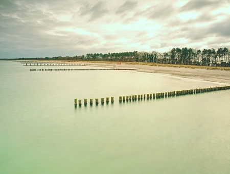 Sandy beach in silent bay, old wooden breakwaters built to protect offshore.  Cloudy sky within...