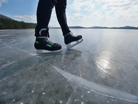 Man ice skating on frozen lake. Thin ice with deeep cracks below man legs.の写真素材