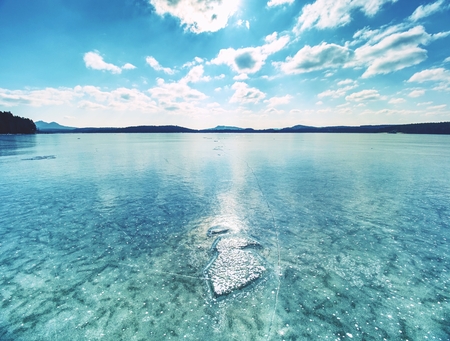 Shining piece of clear ice on frozen lake. Cracks inside many reflections of sun rays. Beauty of winterの写真素材
